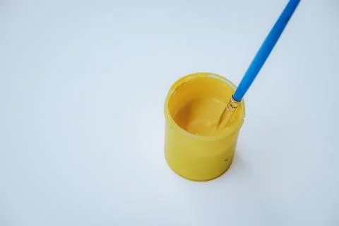 A brush with a blue handle, sitting in a small yellow paint. Photos