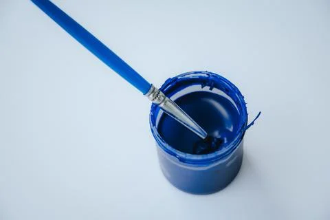 A brush with a blue handle, sitting in a small blue paint. Photos