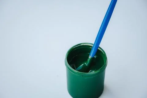 A brush with a blue handle, sitting in a small green paint. Photos