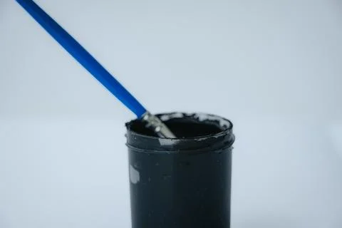 A brush with a blue handle, sitting in a small black paint. Photos
