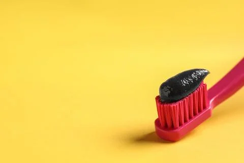 Brush with charcoal toothpaste on yellow background. Space for text Stock Photos