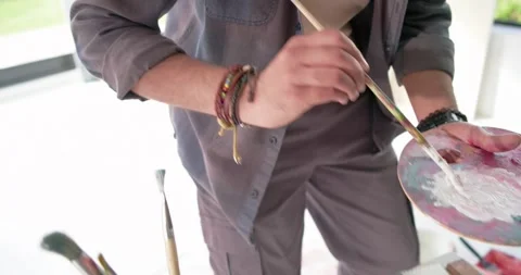 Brush is dipping into white paint jar and mixing on palette, then edging canvas Stock Footage 342392540