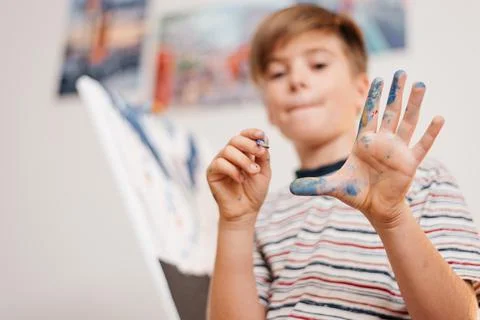 Brush with paints in the hands of a boy while drawing on canvas Stock Photos