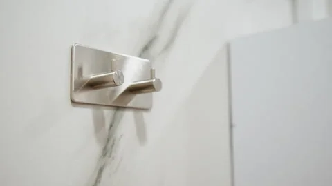 Brushed metal double robe hook mounted on white marble wall with angled empty Stock Footage 345656208
