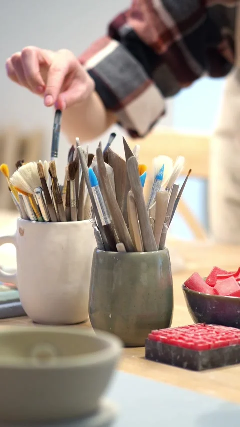 Brushes, stacks, scrapers in a mug on a table with glaze color samples in a pott Stock Footage 311426740