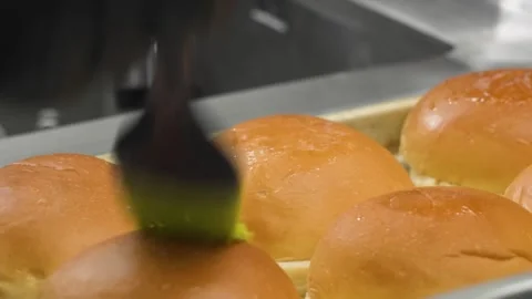 Brushing melted butter or glaze on fresh baked golden burger buns with a silicon Stock Footage 331633776