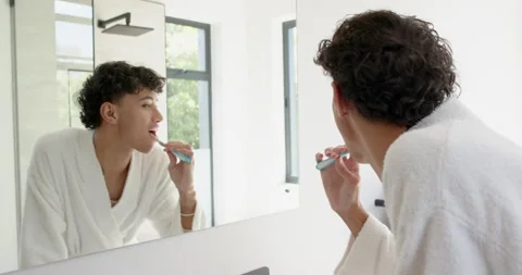 Brushing teeth, person in bathrobe looking in mirror in bright bathroom Stock-Footage 297528367