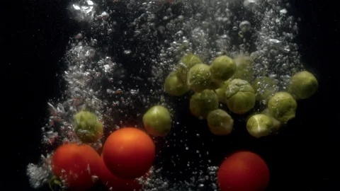 Brussels sprouts and tomatoes falling into the water with a splash Stock Footage 123579212