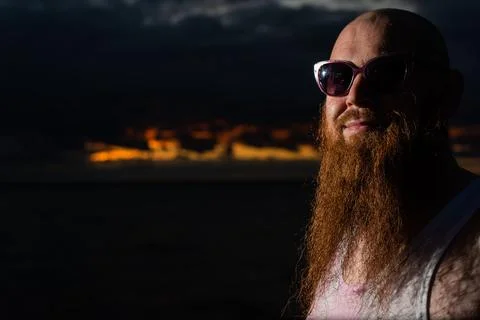 A brutal bald man posing on the beach at sunset parody glamorous chick 스톡 사진