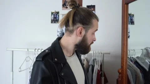 Brutal beard man in a Leather Jacket  is looking in a mirror Untwisting his hair Video stock 147896392