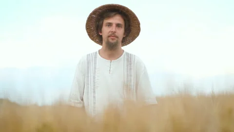 A brutal man with a beard and a straw hat stands in a wheat field with his hands Video stock 135763924