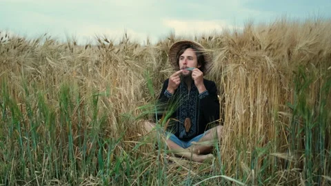 A brutal man with a beard and a straw hat sits in the wheat playing an ancient Stock Footage 136823865