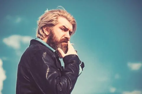 Brutal man with beard on blurry background sky smoking and loking in kamera. Foto stock
