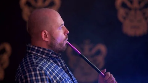 A brutal man with a beard in a plaid blue shirt smoking a water pipe Stock Footage 75262002