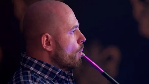 A brutal man with a beard in a plaid blue shirt smoking a hookah shisha Stock Footage 75262018