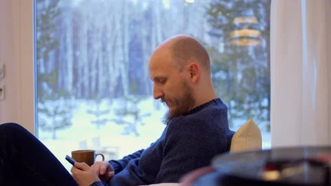A brutal man with a beard sits on the couch at home, uses the Internet through a Stock-Footage 172484580
