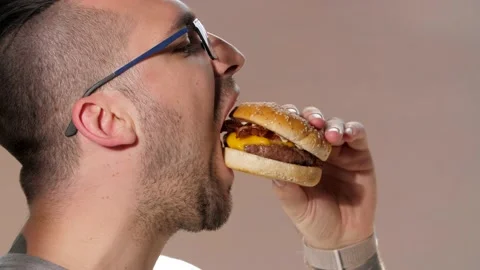 Brutal man bites and eats juicy tasty burger or fast food. Close-up. Video stock 131255389
