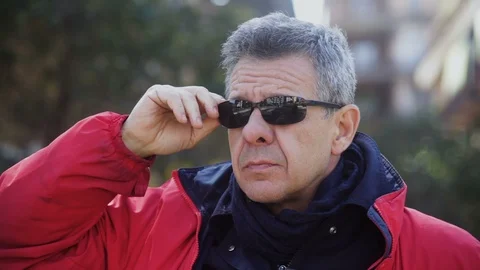 Brutal Man in a red Jacket raises sunglasses and looks around Vidéo 100947119