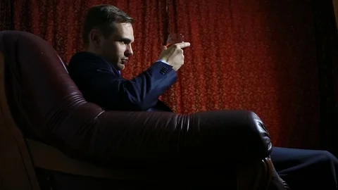 A brutal man in a suit sits in a leather armchair with a glass of alcohol, looks Stock Footage 74755805