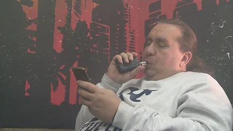 Brutal man typing a message on the phone and vaping Stockbeeldmateriaal 72139726