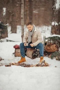 A brutal man in the winter forest by the fire drinking coffee Foto stock