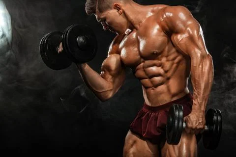 Brutal strong muscular bodybuilder athletic man pumping up muscles with dumbbell Stock Photos