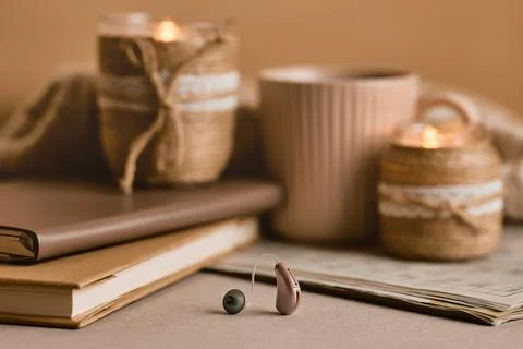 BTE hearing aid rests on a table beside cozy candles, coffee, and books, symb Stockfoto's