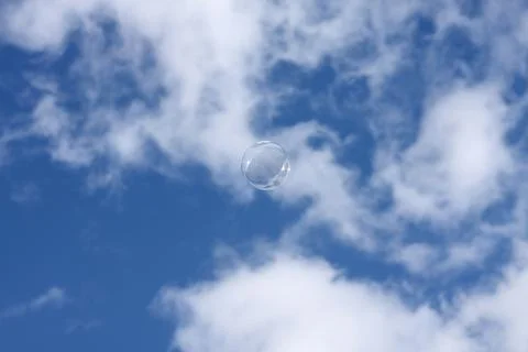 Bubble floating in a blue sky with soft white clouds Stock Photos