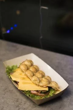 A bubble waffle stuffed with melted cheese and slices of ham is presented on  Stock Photos
