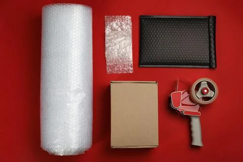 Bubble wrap with cardboard box, padded envelope and tape dispenser on red bac Stock Photos
