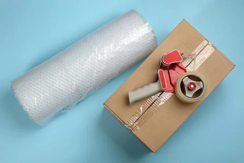 Bubble wrap roll, cardboard box and tape dispenser on turquoise background, f Stock Photos