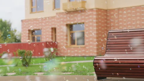 Bubbles Float Across Courtyard Near Bench and Brick Building Vídeos de archivo 328354119