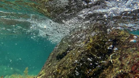 Bubbles float and swirl under ocean waves, illuminated by filtered light in a Video stock 311046247