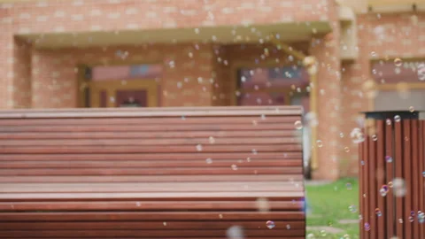 Bubbles Floating Across Courtyard Near Bench and Brick Building Vídeos de archivo 321482262