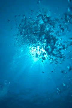 Bubbles going to the water surface with sunrays in the background. Stock Photos