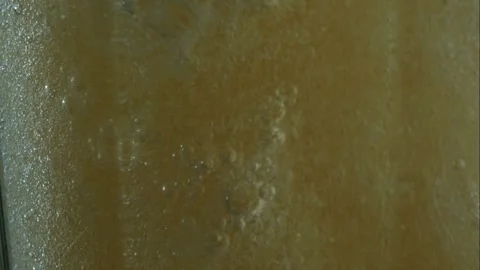 Bubbles rise and foam forms in a glass of carbonated golden liquid Stock Footage 326628051