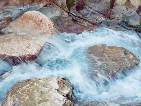 A bubbling foamy river flows over large rocks. Closeup photo Stock Photos