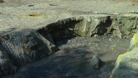 Bubbling geothermal mud pool surrounded by mineral deposits and eroded ground Stock Footage 340503923