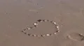 bubbly wave washes over stone pebble heart in sand HD Footage