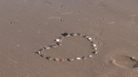 Bubbly wave washes over stone pebble heart in sand Stock Footage 42741496