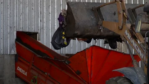 The bucket of a bulldozer dumps garbage onto a conveyor belt inside a Stock Footage 210451431