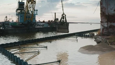 The bucket of a floating crane unloads sand into the water, with an old Stock Footage 217406440