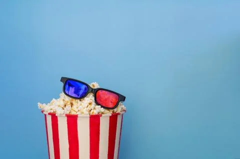 A bucket full of popcorn on a blue background and 3D glasses. Stock Photos