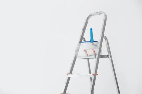 Bucket with paint and roller on step ladder near white wall Stock Photos