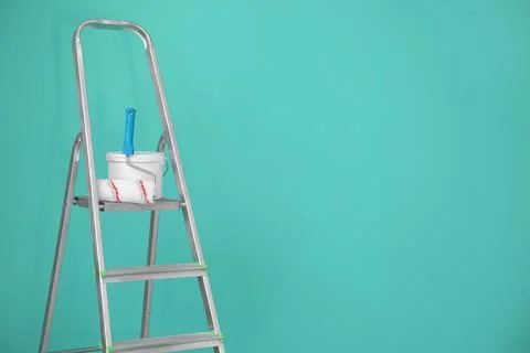 Bucket with paint and roller on step ladder near color wall Stock Photos
