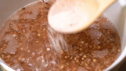Buckwheat in boiling water, cooked in a pan. Salted with a wooden spoon Stock Footage 248180960
