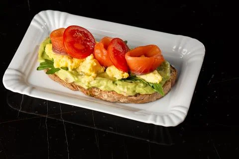 Buckwheat bread toast with an egg, a sliced avocado, a salmon, tomatoes and l Stock Photos