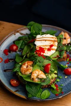 Buckwheat bread toasts with a poached egg, a sliced avocado, a shrimps, tomat Stock Photos