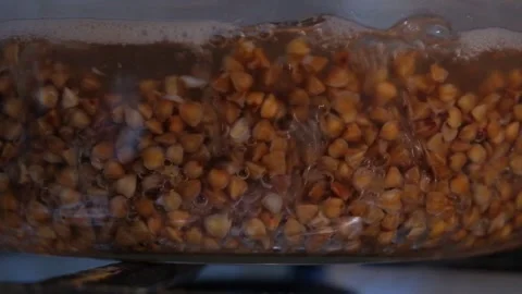 Buckwheat is cooked in a transparent pan. Buckwheat is cooked close-up. Cooking Stock Footage 307314167