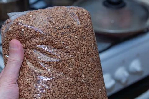 Buckwheat grains in a transparent plastic package held by a hand in the kitch 스톡 사진